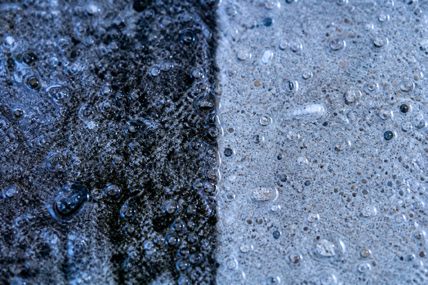 Close-up of concrete split down the middle: black algae staining on one side, clean wet aggregate on the other